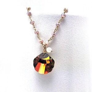 May include: A gold chain necklace with a brown and yellow crystal pendant in the shape of a seashell. The chain is made of small gold beads and pink beads.