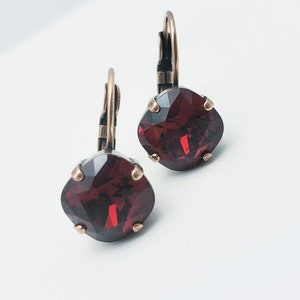 Op de afbeelding: Een paar oorbellen met een donkerrode vierkante kristal en een bronzen haak.