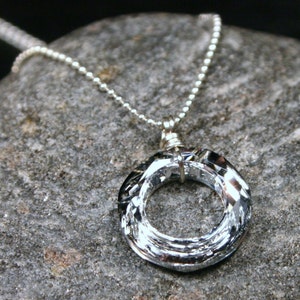 May include: A silver chain necklace with a silver crystal pendant in the shape of a circle. The pendant has a faceted design and is suspended from the chain by a silver wire.