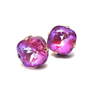May include: A pair of purple square-shaped earrings with a gold setting. The earrings have a faceted design and a shimmery finish.