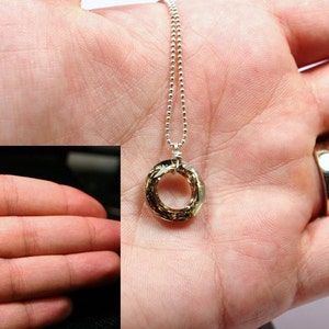 May include: A silver chain necklace with a gold-toned pendant. The pendant is a circle with a textured surface.