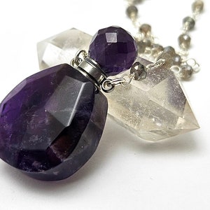 May include: A silver chain necklace with a faceted amethyst crystal bottle pendant. The bottle is topped with a faceted amethyst crystal stopper. The chain is made of silver beads and is approximately 20 inches long.