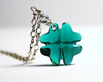 Puede incluir: Un collar de cadena de plata con un colgante de trébol de cuatro hojas de color turquesa.