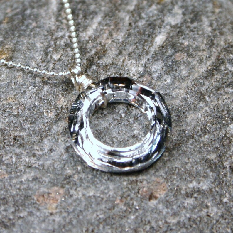 May include: A silver necklace with a circular pendant. The pendant is made of multiple layers of metal, creating a textured, swirling design.