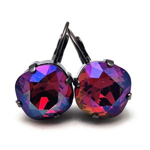 Op de afbeelding: Een paar oorbellen met een donker zilveren afwerking en een grote, gefacetteerde, iriserende edelsteen in een diepe rode en paarse kleur.