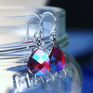 May include: A pair of silver dangle earrings with teardrop-shaped red and blue iridescent crystals.