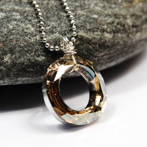 May include: A silver chain necklace with a brown crystal pendant in the shape of a circle. The pendant is faceted and has a shiny finish.
