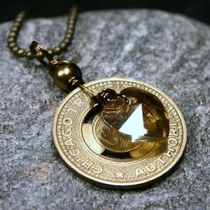 May include: A gold necklace with a pendant made from a vintage Chicago Transit Authority token. The token has a clear crystal in the centre.