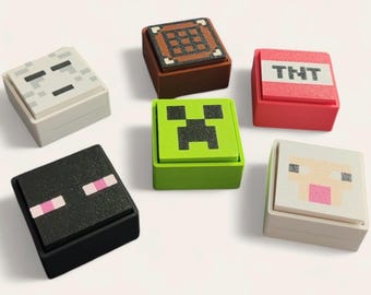 May include: Six square boxes with Minecraft designs. The boxes feature pixelated images of a skeleton, crafting table, TNT block, Creeper, Enderman, and sheep. The boxes are in various colours, including white, brown, red, green, and black.