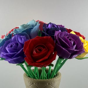 May include: A bouquet of colorful artificial roses in a decorative vase. The roses are in shades of red, purple, blue, and yellow, with green stems. The vase is a light brown color.