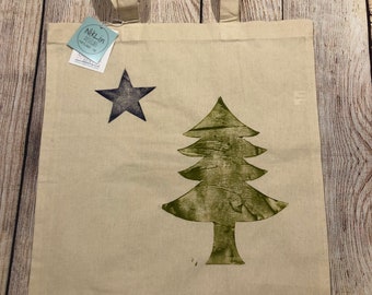 May include: A beige canvas tote bag with a blue star and a green tree design. The bag has the text "NikLin Designs" printed on the bottom.