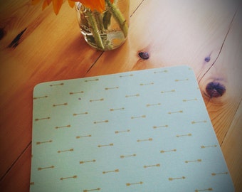 May include: A light blue square placemat with a pattern of gold arrows. The placemat is on a wooden table.