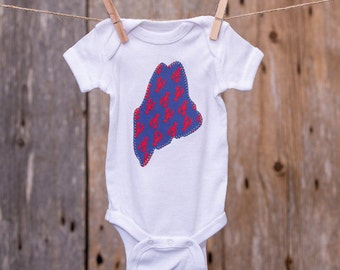 May include: White baby onesie with a blue and red applique of the state of Maine with lobsters on it.