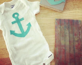 May include: A white baby onesie with a teal anchor graphic. The onesie has a snap closure at the bottom.