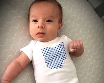 May include: A baby wearing a white onesie with a blue and white geometric pattern in the shape of the state of Ohio.
