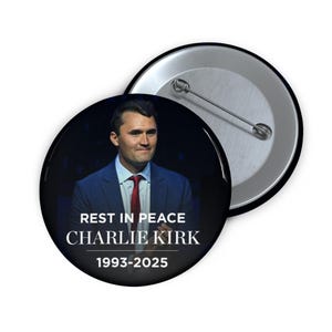 May include: A circular badge featuring a portrait of a man in a suit and tie. The text "REST IN PEACE CHARLIE KIRK 1993-2025" is displayed in white. The badge is black with a silver pin back.