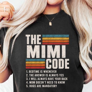 Puede incluir: Camiseta negra con el texto "THE MIMI CODE" en una fuente blanca desgastada. El diseño incluye un bloque de color retro con el texto "1. LA HORA DE DORMIR ES CUANDO SEA, 2. LA RESPUESTA ES SIEMPRE SÍ, 3. SIEMPRE TE CUBRIRÉ, 4. MAMÁ NO NECESITA SABERLO, 5. LOS ABRAZOS SON OBLIGATORIOS."