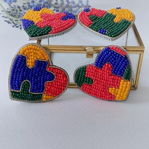 Könnte beinhalten: Vier herzförmige Perlenohrringe mit einem Puzzle-Design. Die Ohrringe sind aus roten, blauen, grünen und gelben Perlen gefertigt.