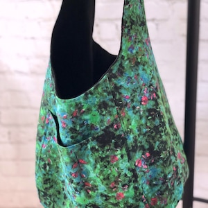 May include: A green and black tote bag with a floral print. The bag has a large pocket on the front and a black lining.