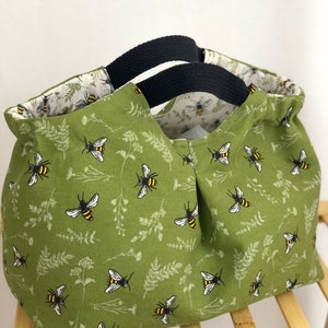 May include: A green canvas tote bag with black handles. The bag has a bee and floral pattern.