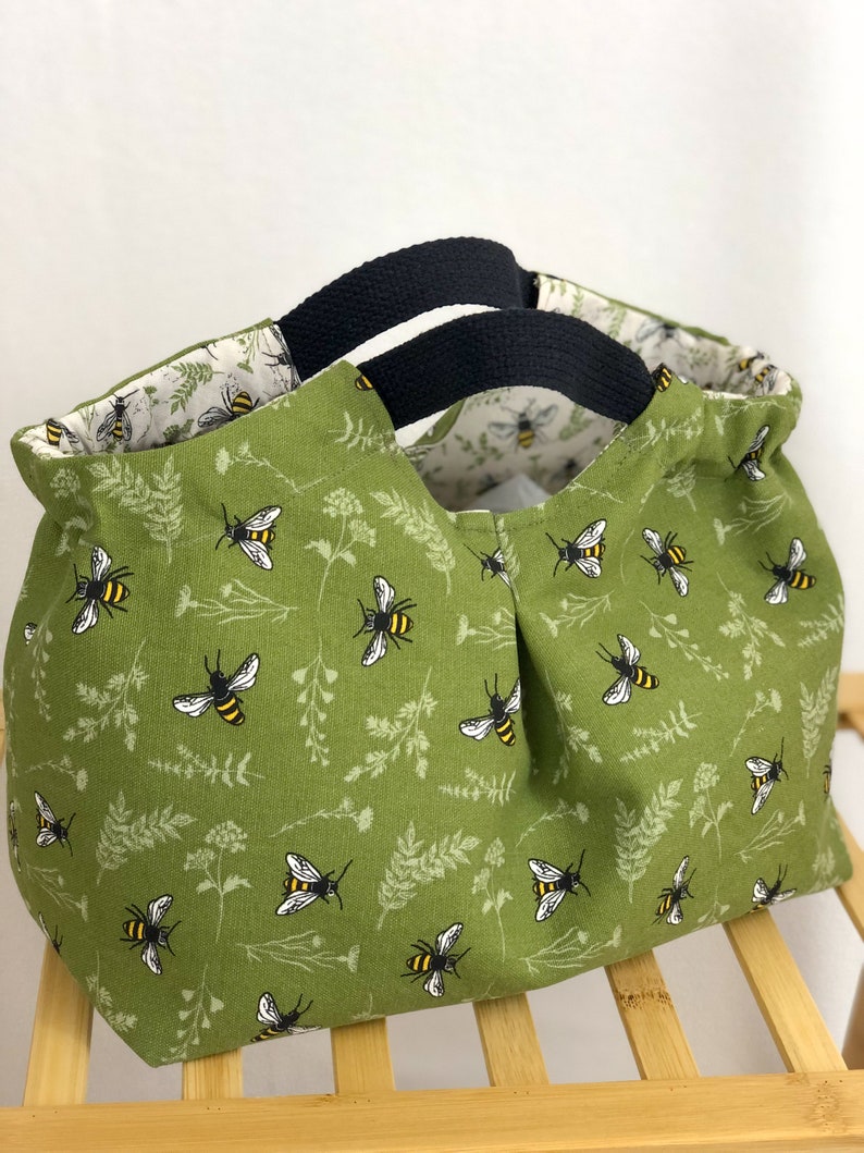 May include: A green canvas tote bag with black handles. The bag has a bee and floral pattern.