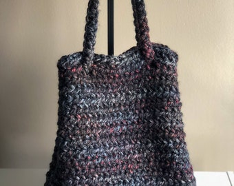 Puede incluir: Una bolsa de mano de crochet negra, gris y roja con dos asas largas.