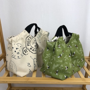May include: Two reusable shopping bags. One is beige with black straps and a vintage French postage stamp design. The other is green with black straps and a bee pattern.