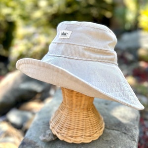 May include: A light beige corduroy sun hat with a wide brim. The hat has a small label on the front that says "Blue Corduroy".