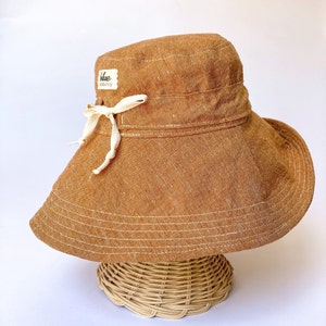May include: A brown wide-brimmed sun hat with a white ribbon and a small label that says "blue meadow" on it.