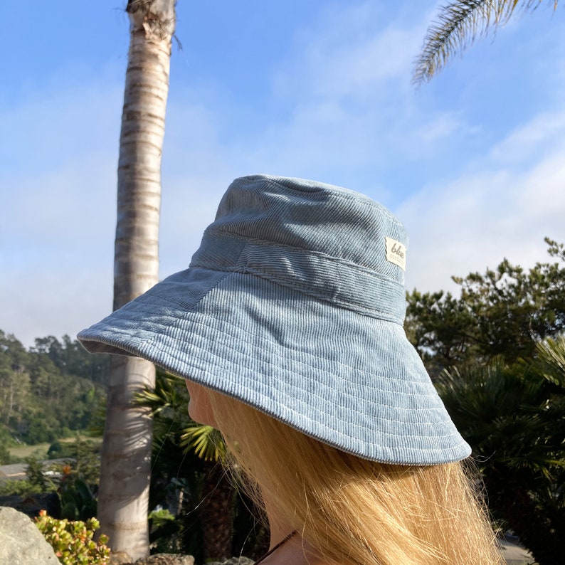 Pu&ograve; includere: Un cappello a secchiello in velluto a coste blu chiaro con un'ampia tesa. Il cappello ha una piccola etichetta sul lato che dice "below".