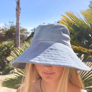 Pu&ograve; includere: Un cappello a secchiello in velluto a coste blu chiaro con un'ampia tesa. Il cappello &egrave; indossato da una persona con lunghi capelli biondi.