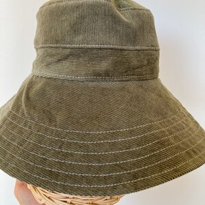 K&ouml;nnte beinhalten: Ein gr&uuml;ner Cord-Bucket-Hut mit breiter Krempe und wei&szlig;en N&auml;hten.