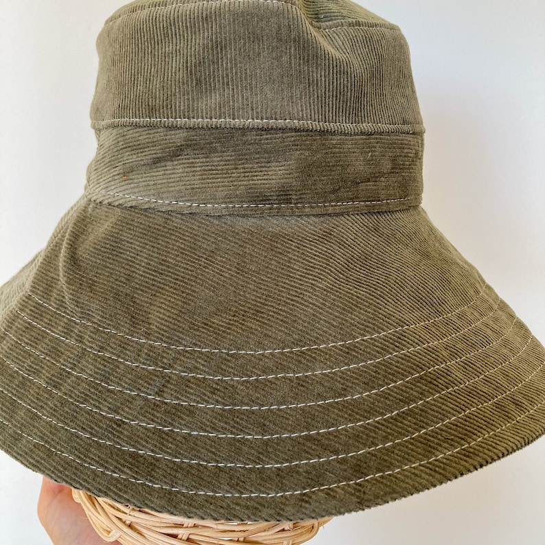K&ouml;nnte beinhalten: Ein gr&uuml;ner Cord-Bucket-Hut mit breiter Krempe und wei&szlig;en N&auml;hten.