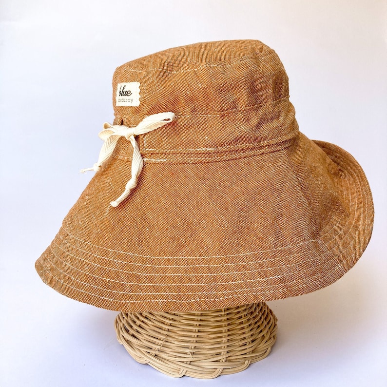 May include: A brown wide-brimmed sun hat with a white ribbon and a small label that says "blue meadow" on it.