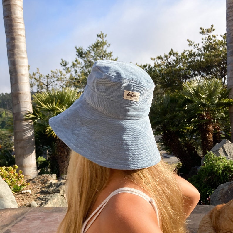 Pu&ograve; includere: Un cappello a secchiello in velluto a coste blu chiaro con un'etichetta marrone che dice "blue corduroy".