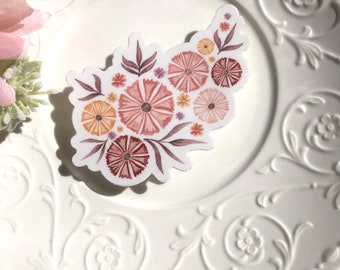 May include: A sticker featuring a cluster of pink, orange, and brown flowers with purple and yellow accents. The flowers are arranged in a loose, organic shape, and the sticker is printed on a white background.