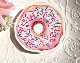 May include: A pink iced donut with colourful sprinkles. The donut is on a white background.