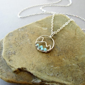 May include: A silver chain necklace with a wire-wrapped pendant featuring a mountain silhouette and turquoise beads.