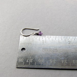 K&ouml;nnte beinhalten: Ein silberner Ohrring mit einem kleinen, hellvioletten Edelstein. Der Ohrring ist neben einem Lineal abgebildet und misst etwa 1,2 cm in der L&auml;nge.