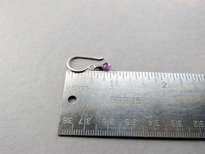 K&ouml;nnte beinhalten: Ein silberner Ohrring mit einem kleinen, hellvioletten Edelstein. Der Ohrring ist neben einem Lineal abgebildet und misst etwa 1,2 cm in der L&auml;nge.
