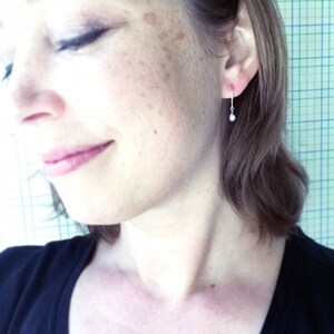 K&ouml;nnte beinhalten: Nahaufnahme eines Ohrs mit einem kleinen silbernen Ohrring mit einer einzelnen Perle, die daran h&auml;ngt.