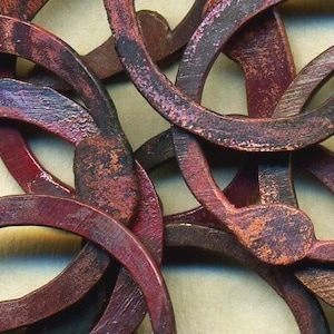 May include: A close-up of a group of interconnected metal rings, each with a unique shape and a reddish-brown patina. The rings are intertwined and layered, creating a complex and intricate design.