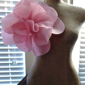 May include: A pink fabric flower with multiple layers, attached to a light brown mannequin.