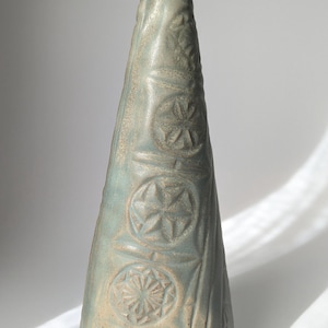 May include: A ceramic cone-shaped sculpture with a light blue glaze and intricate geometric designs.