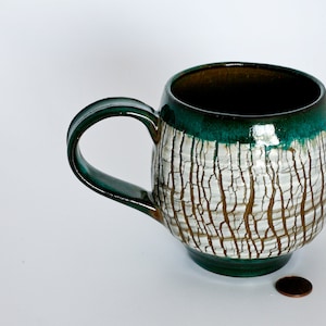 May include: A white ceramic mug with a green glaze and a crackled finish. The mug has a rounded body and a handle.
