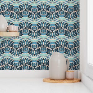 May include: A close-up of a wallpaper with a repeating pattern of stylized floral shapes in shades of blue and teal, outlined in white. A white pitcher, a small wooden coaster, and a small cup are in the foreground.