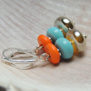 May include: Silver dangle earrings with three beads. The beads are orange, turquoise, and gold.