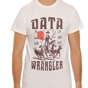 Może przedstawiać: Biały t-shirt z grafiką w stylu vintage przedstawiającą kowboja na koniu łapiącego wykresy danych lasso. Pod grafiką znajduje się napis "DATA WRANGLER".