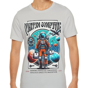 Puede incluir: Una camiseta gris claro con un gráfico colorido de un astronauta sosteniendo cajas en el espacio. El gráfico incluye el texto "Quantum Computing" y "Making parallel universes jealous since its invention."