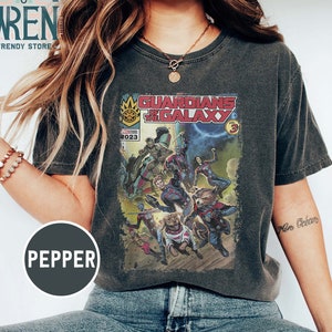 Pu&ograve; includere: Una maglietta grigia scura con un design di fumetto vintage con i Guardiani della Galassia. La copertina del fumetto presenta il testo "Guardians of the Galaxy" e "Vol. 3".
